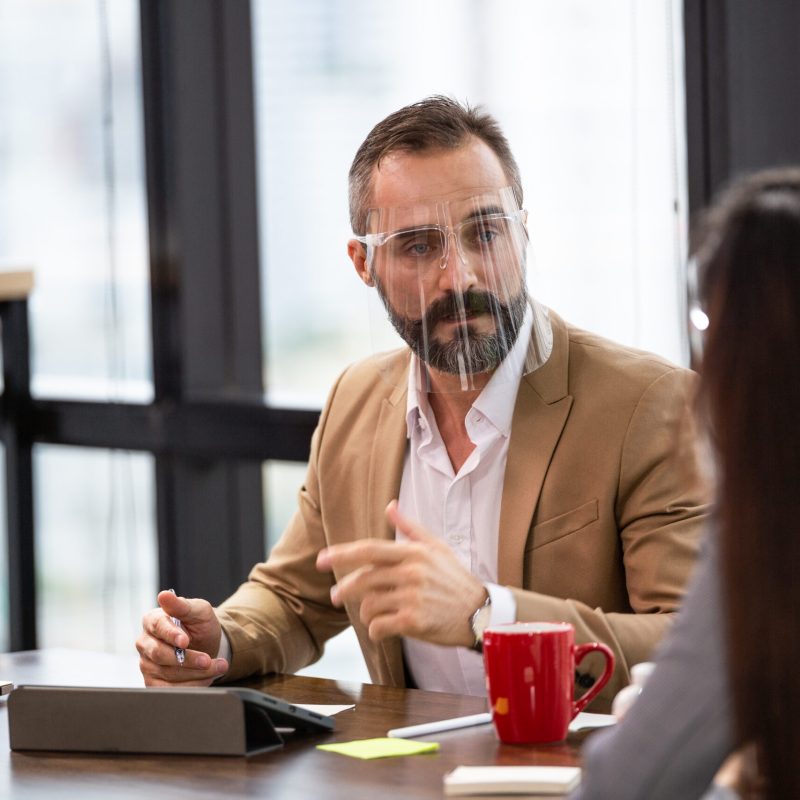 Caucasian business man wearing face shield discussing and brainstorming with team in co-working space or office meeting room. partnership people working together, project dealing with customer